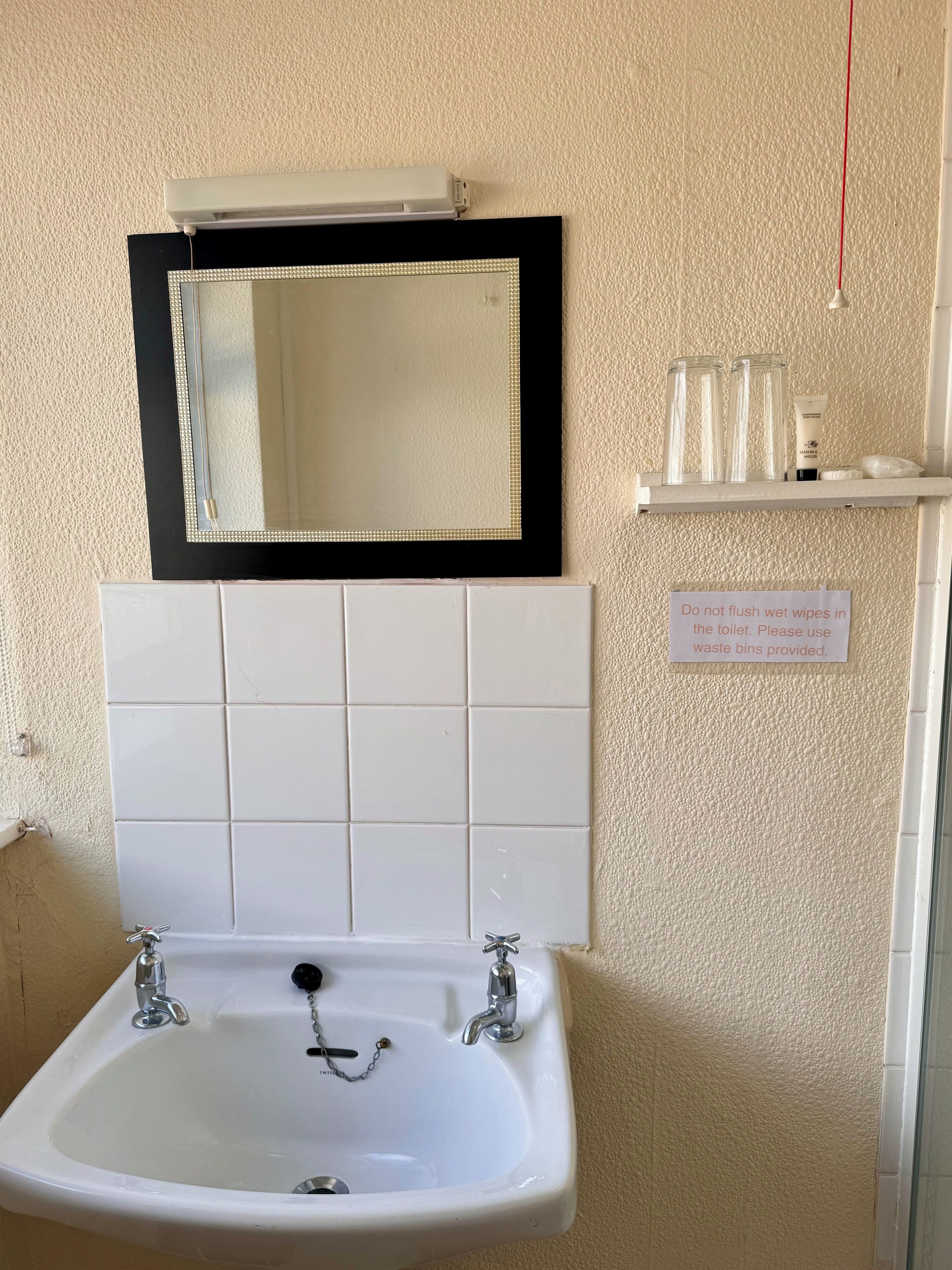 A bathroom with a white sink, a mirror with a black frame, and a sign instructing not to flush wipes in the toilet.