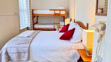 A bedroom with a bunk bed, a single bed, a bedside table with a lamp, a mirror, and a hairdryer.