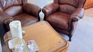 A room with two brown leather armchairs, a wooden coffee table with a tray holding two white mugs and a small box, and a wooden cabinet in the background. - Kendal Hotel (Blackpool)