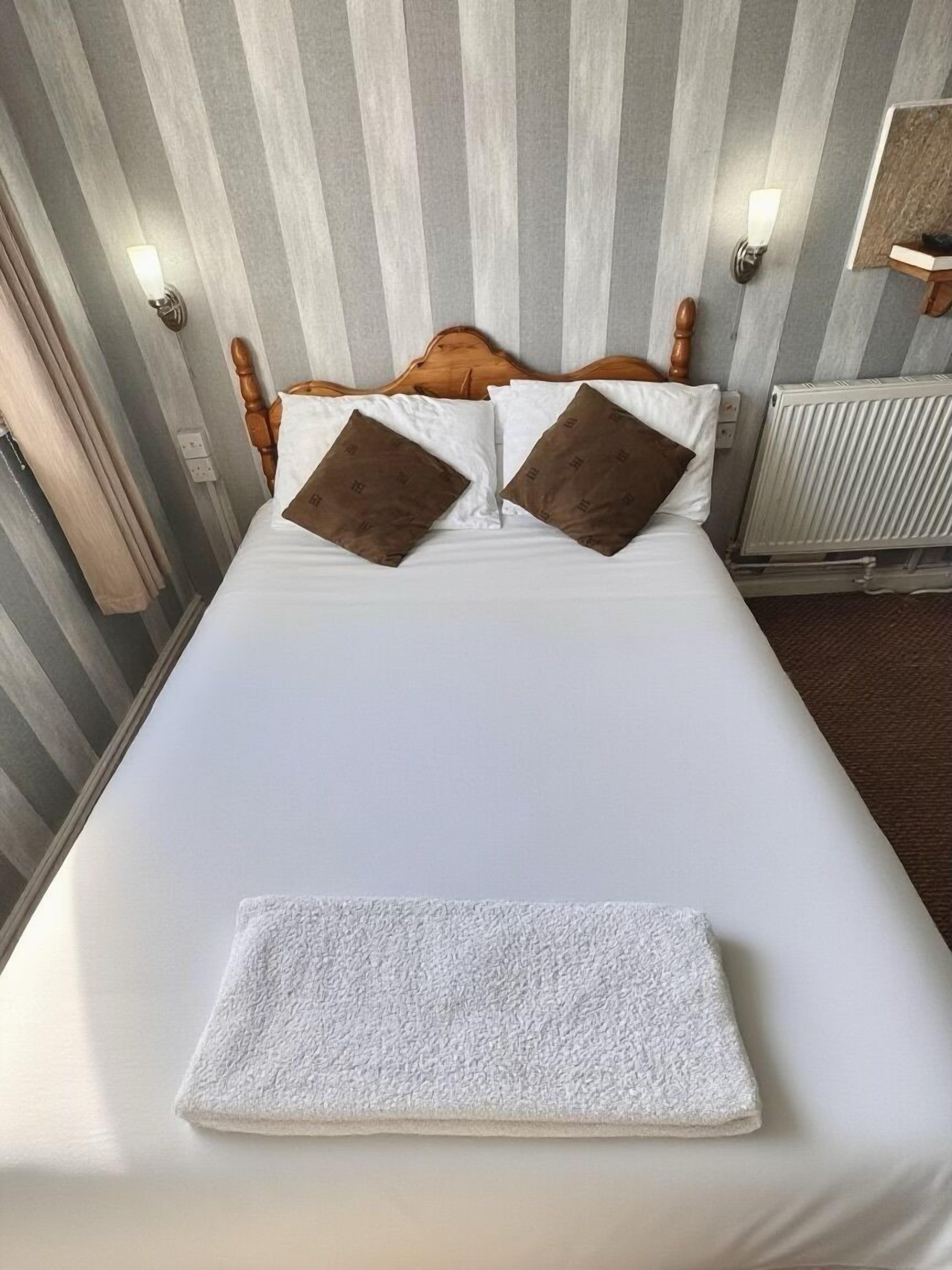 A neatly made bed with white linens and two brown pillows, a white towel on the bed, and a striped wall in the background.