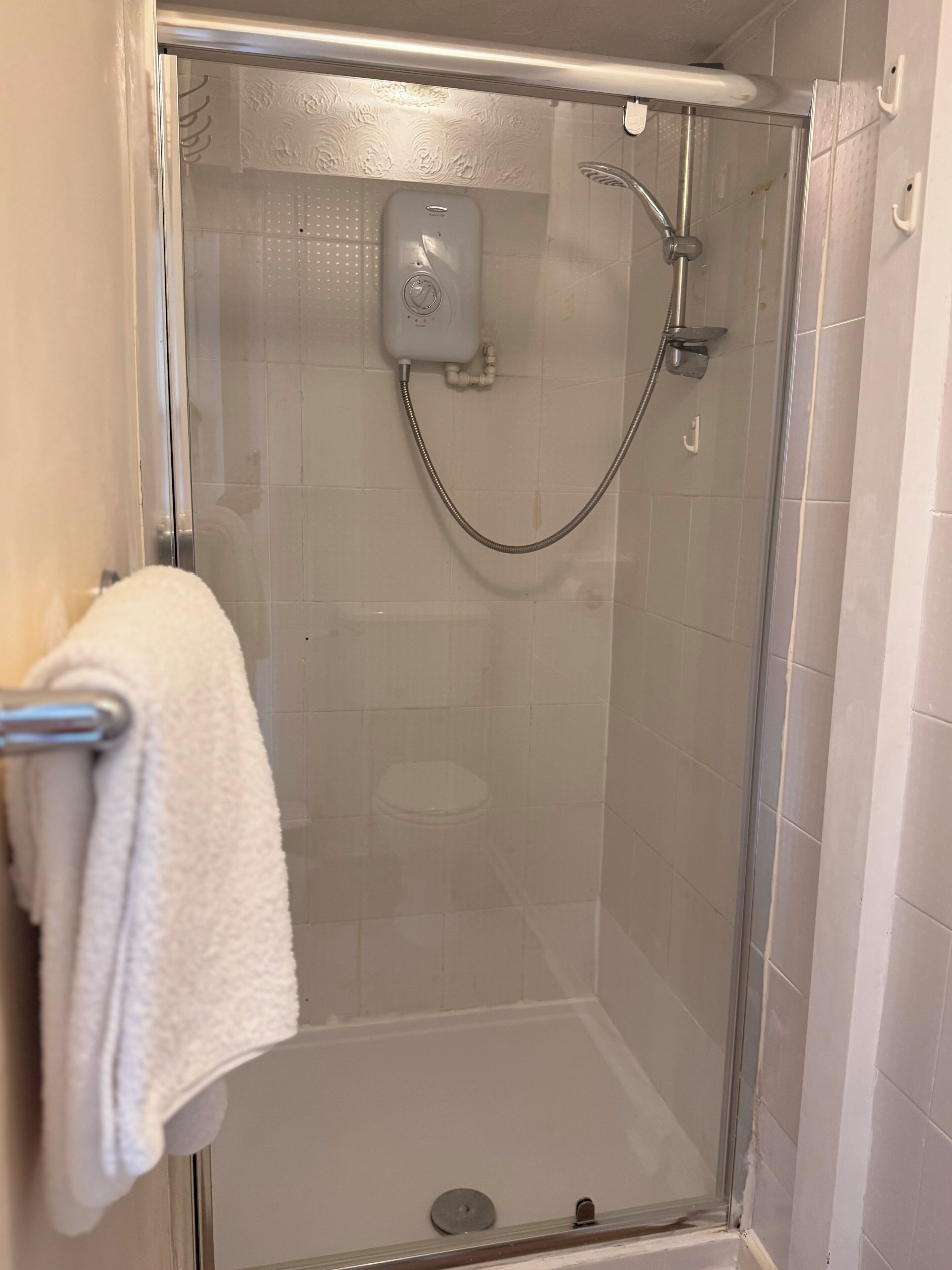 A glass-enclosed shower with a handheld showerhead and a control panel.