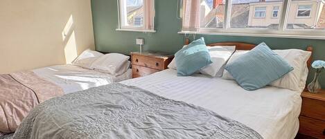 A bedroom with a large bed, two bedside tables, a dresser, and a window with curtains.