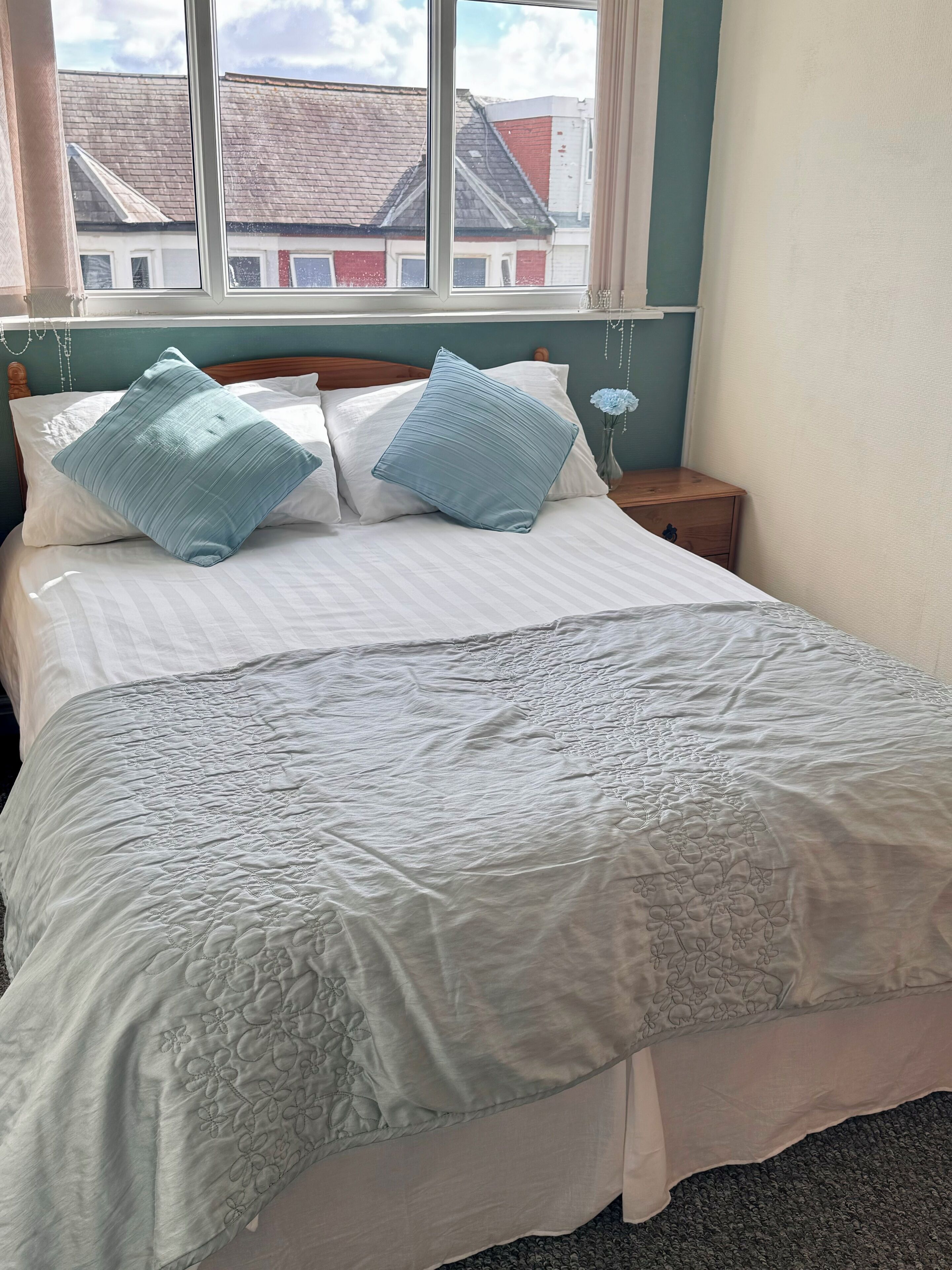 A neatly made bed with a white and light blue quilt, two matching pillows, and a wooden headboard.