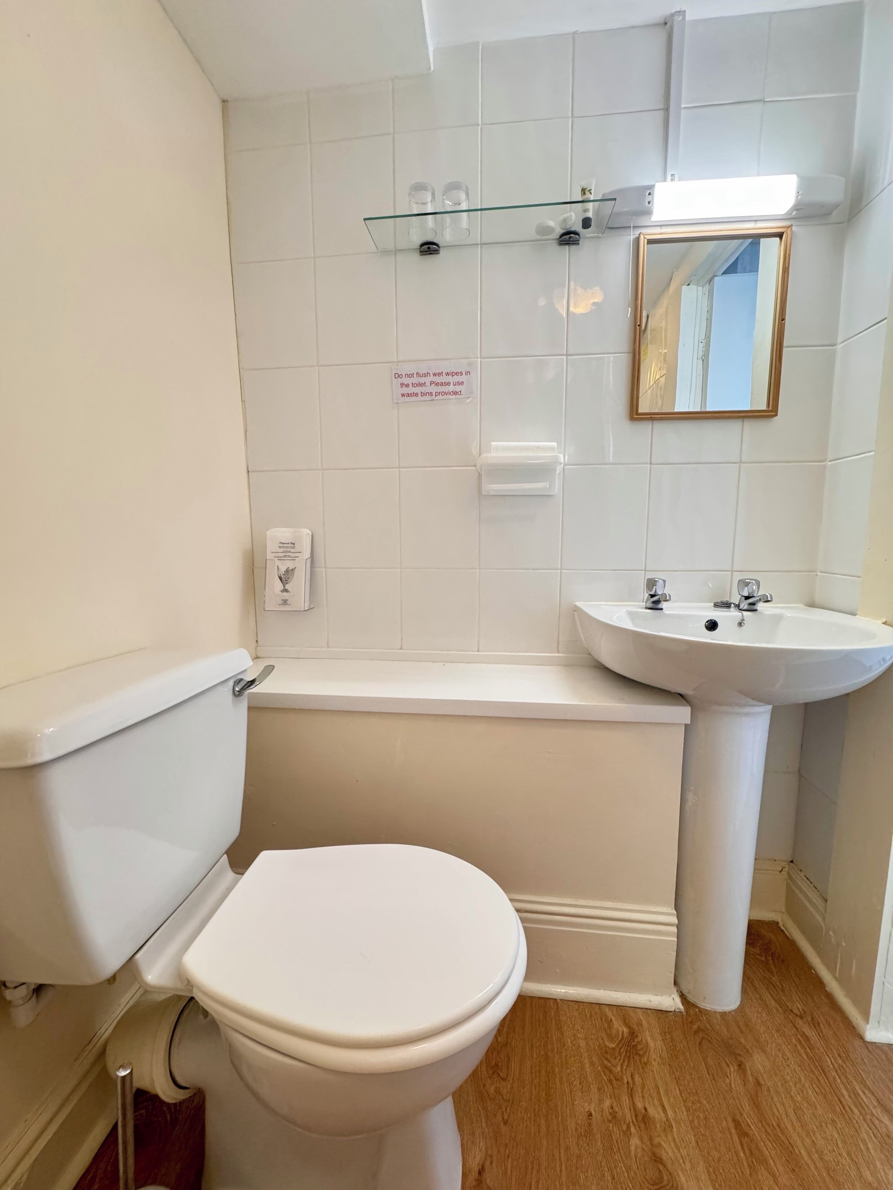 A bathroom with a toilet, a sink, and a bathtub. There is a sign on the wall instructing not to flush wet wipes in the toilet.