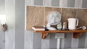A bathroom with a striped wall, a wooden shelf with a fan, a kettle, and a book. - Kendal Hotel (Blackpool)