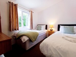Ett sovrum med två sängar, ett fönster med gardiner, ett sängbord med en lampa och ett litet bord vid sängen.