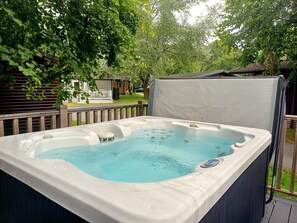 Ett bubbelbad i en trädgård, med ett trädäck och ett vitt staket.