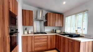Une cuisine moderne avec des meubles en bois, une hotte en acier inoxydable, un four encastré et une fenêtre équipée de stores.