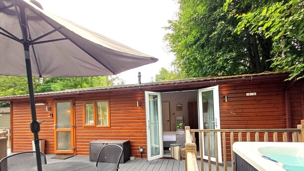 Une cabane en bois dotée d’une terrasse, d’un bain à remous et d’une table avec des chaises.