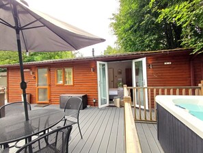 En stuga av trä med en veranda, ett bubbelbad och ett bord med stolar.