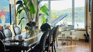 Un espace repas agrémenté d’un piano, de grandes fenêtres et offrant une vue sur un lac.