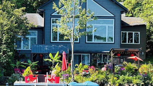 Une maison moderne à deux étages, dotée d’une jetée qui s’avance sur un plan d’eau, et entourée d’une végétation luxuriante.