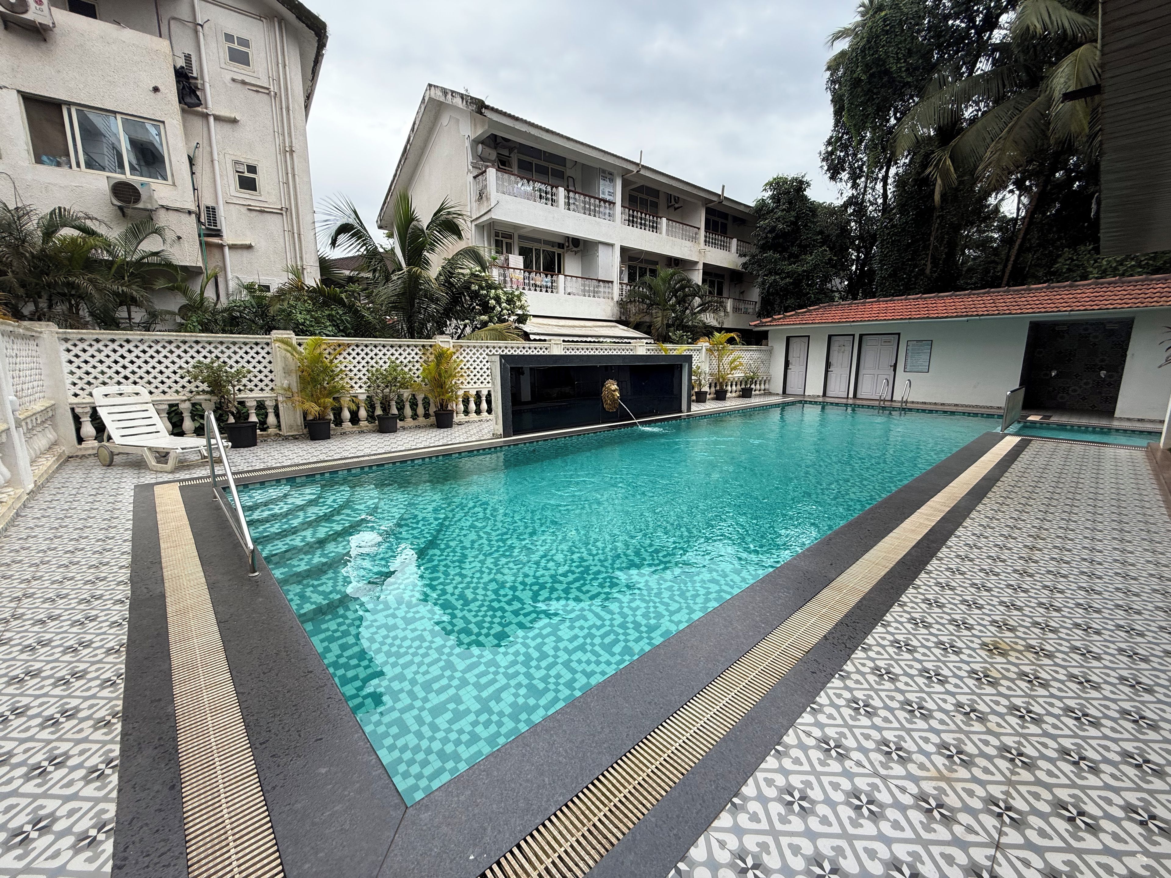 Una piscina con solárium y bordeado por edificios y palmeras.
