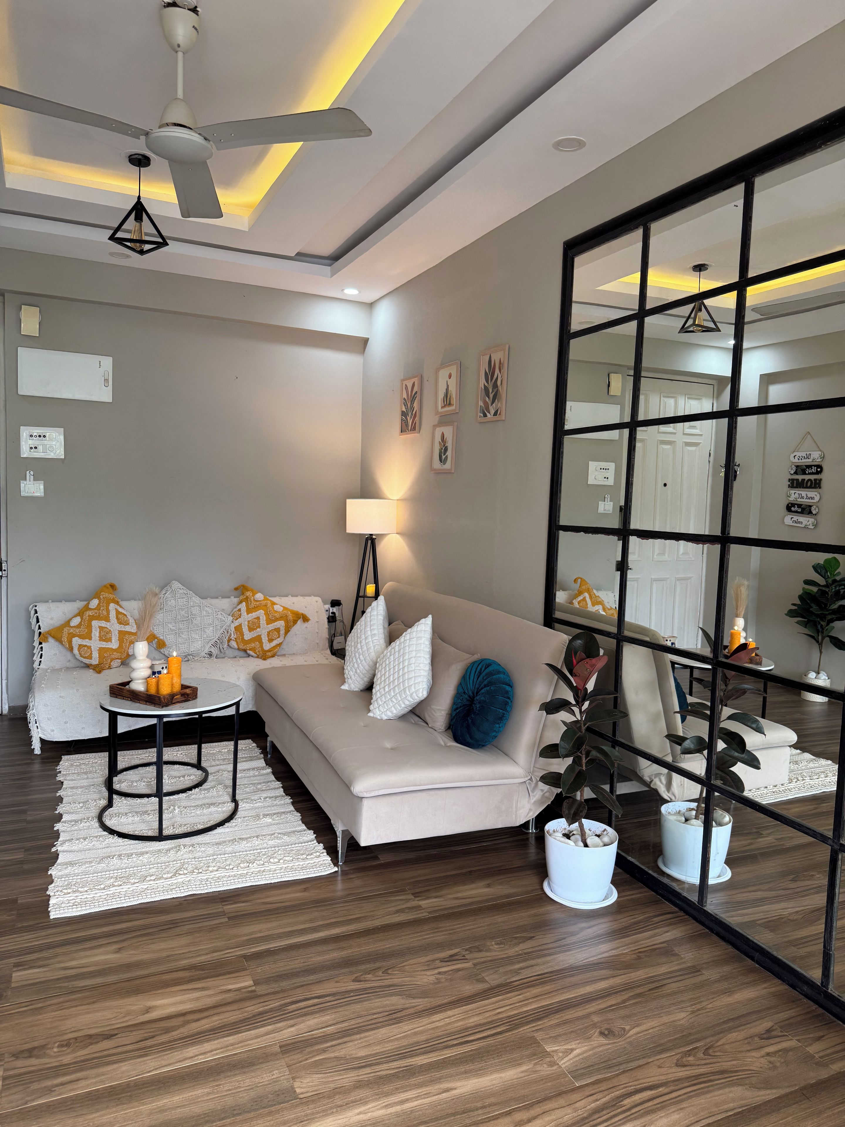 A modern living room with a sofa, a coffee table, and a floor lamp. There is a ceiling fan and a large mirror reflecting the room.