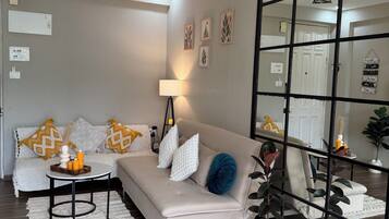 A modern living room with a sofa, a coffee table, and a floor lamp. There is a ceiling fan and a large mirror reflecting the room.