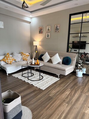 A modern living room with a sofa, coffee table, and decorative items. - Dishney Den- 1BHK - Hill View - Pvt Balcony Bar (Shivoli)