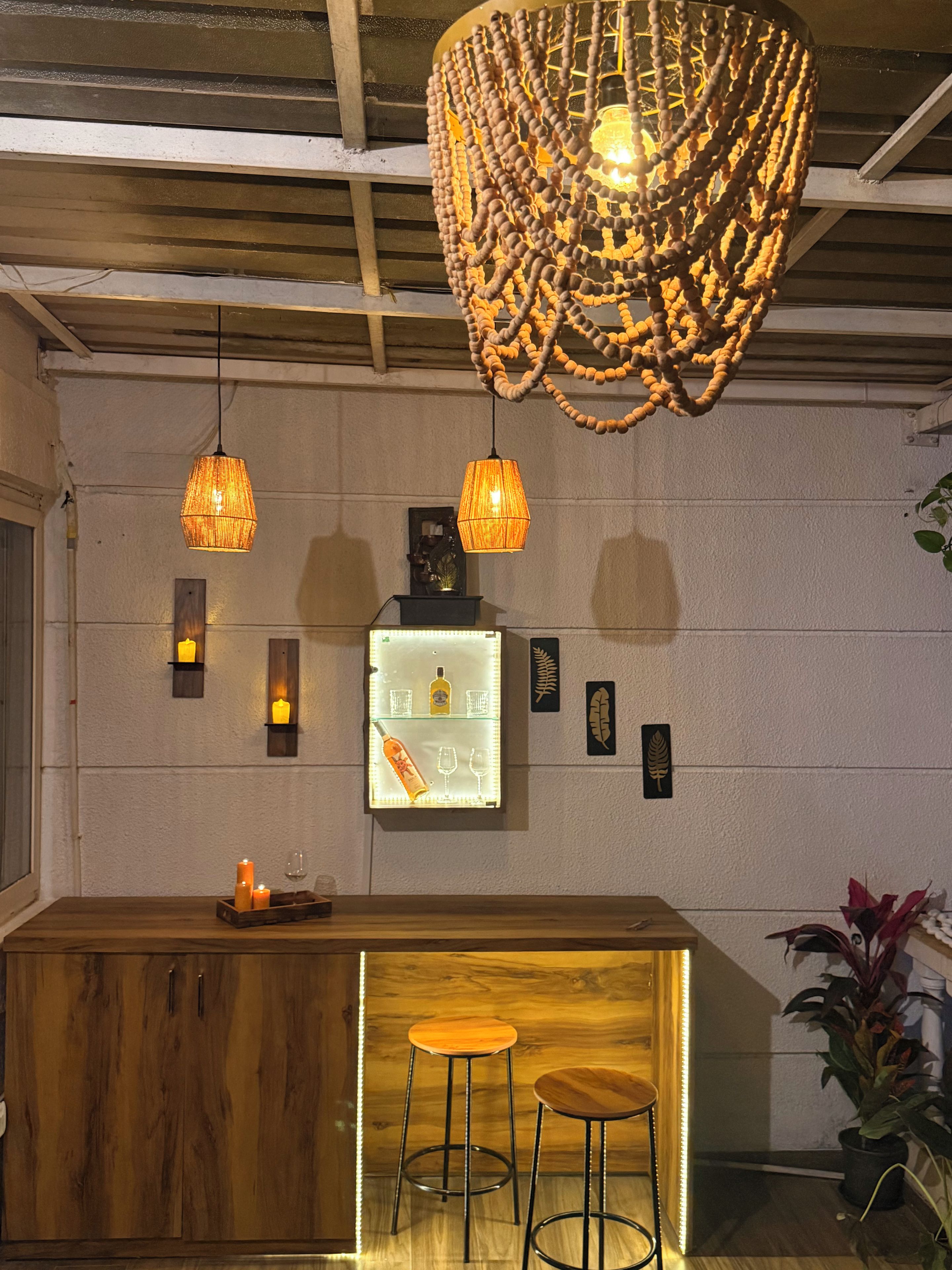 Zona de bar con taburetes de madera, iluminación colgante y una estantería con botellas y vasos.
