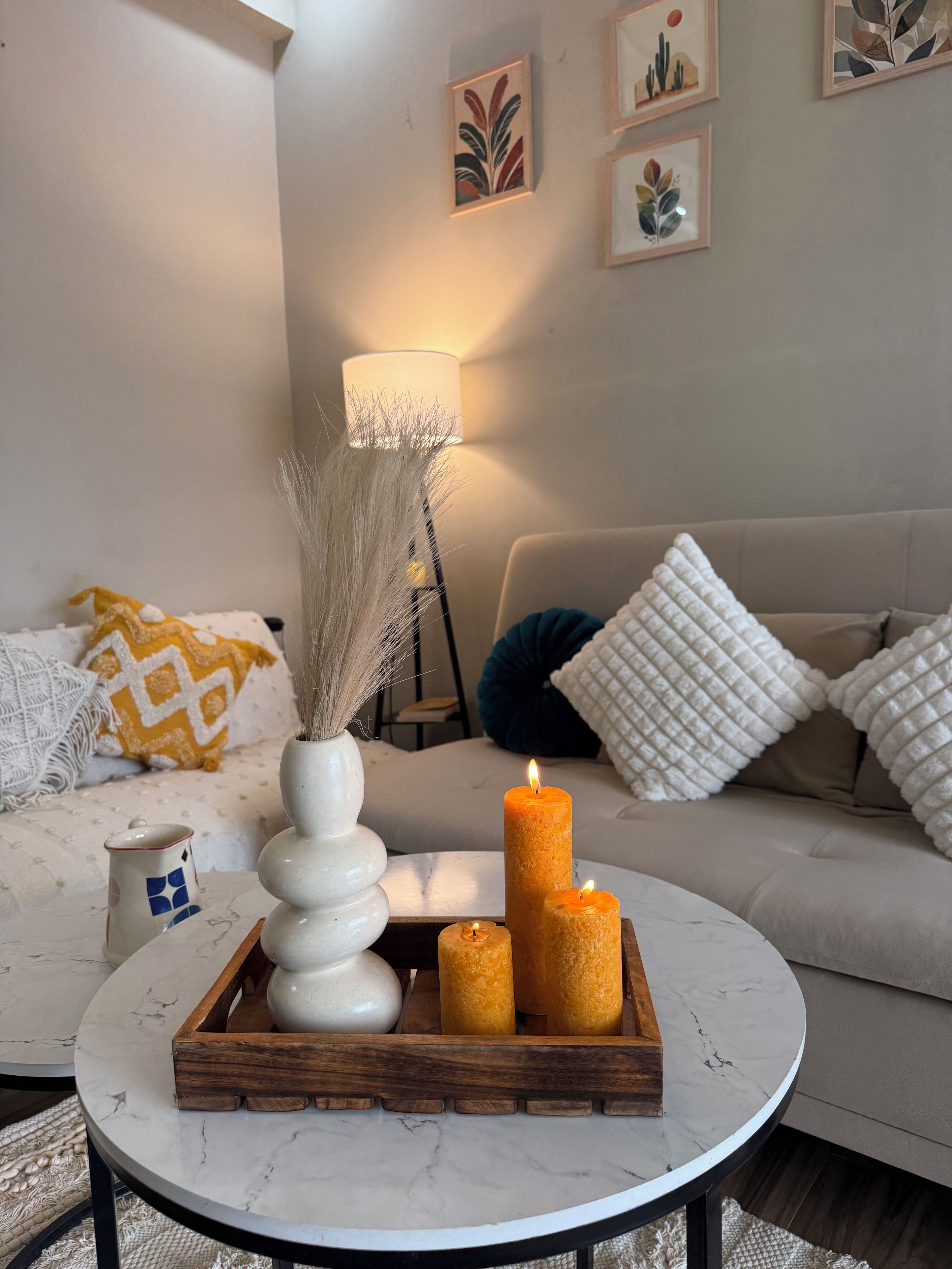A living room with a round table, a vase, candles, and a lamp.