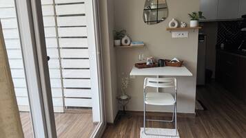 A modern kitchen with a white table, a metal chair, a mirror, and a small side table with a plant.