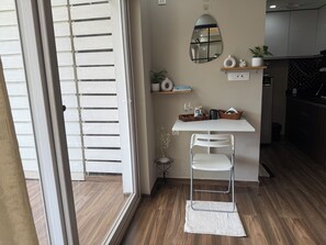 Una cocina moderna con una mesa blanca, una silla de metal, un espejo y una mesita auxiliar con una planta.