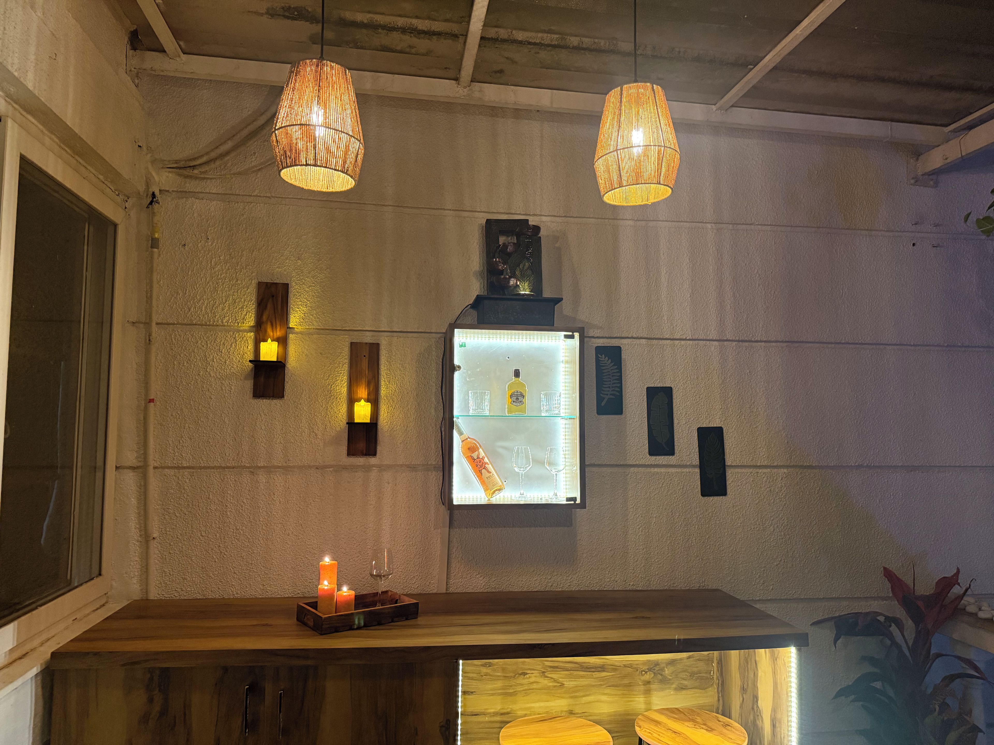 Un'area bar con un bancone in legno, candele e un frigorifero che espone bottiglie e bicchieri.