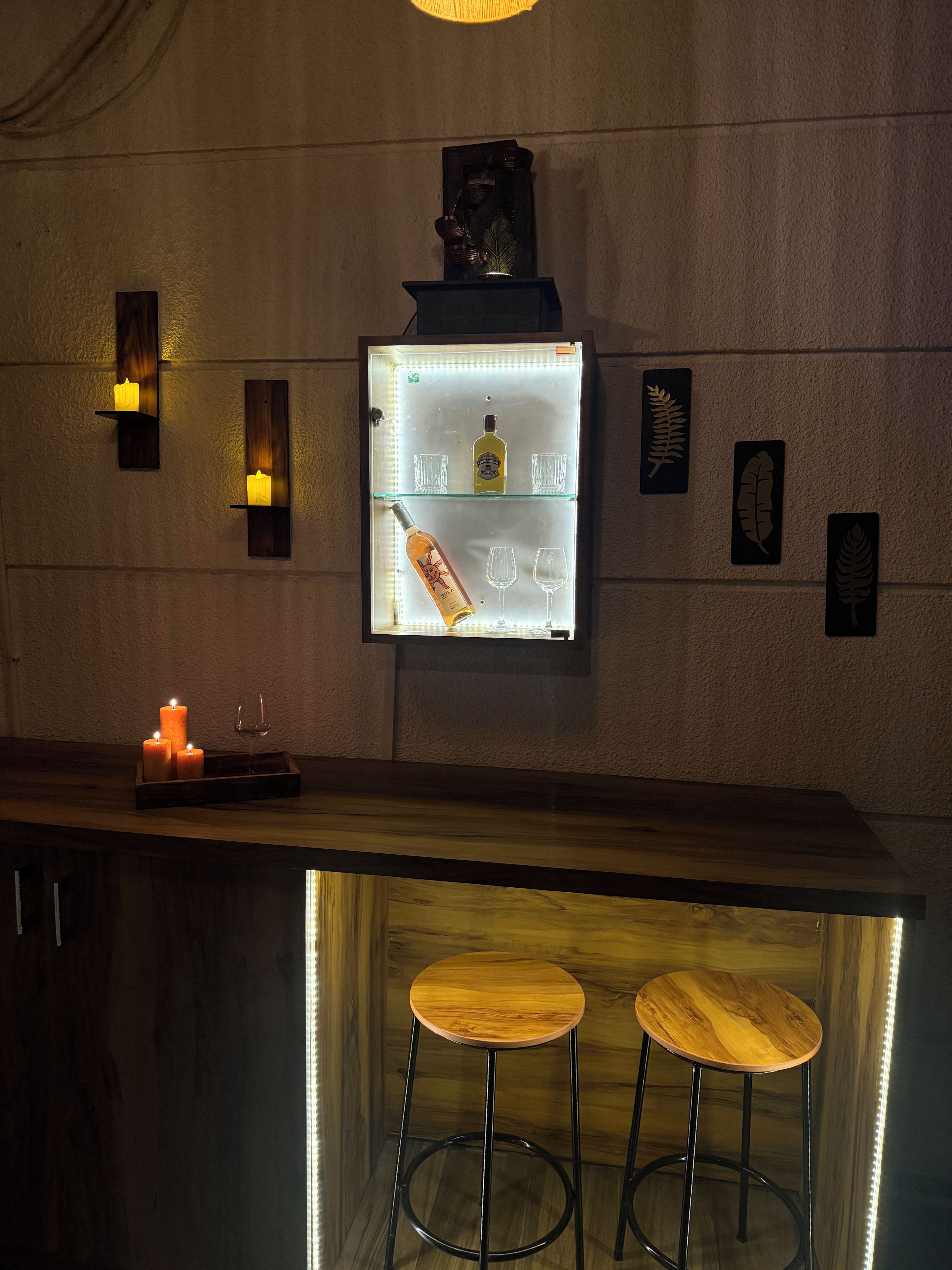 Un espace bar doté d’une vitrine éclairée, de bougies et de tabourets.