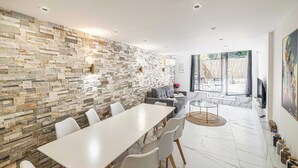 Een moderne eethoek met een stenen muur, een lange tafel, witte stoelen en een bank.