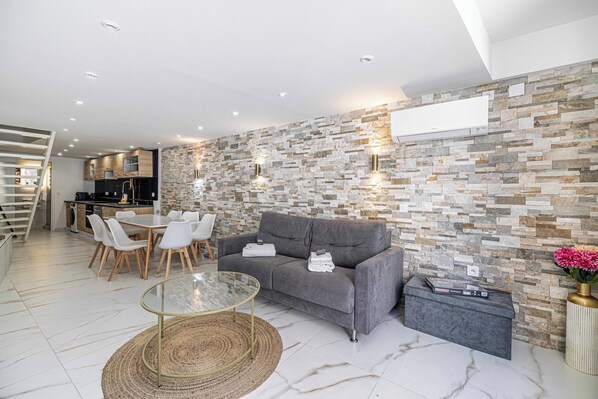 Una sala moderna con un sofá gris, una mesa de centro de cristal y un comedor con sillas blancas.