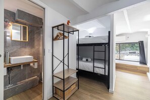 Una habitación moderna con un banco de madera, una cama litera negra, un lavabo blanco y un ventanal grande.