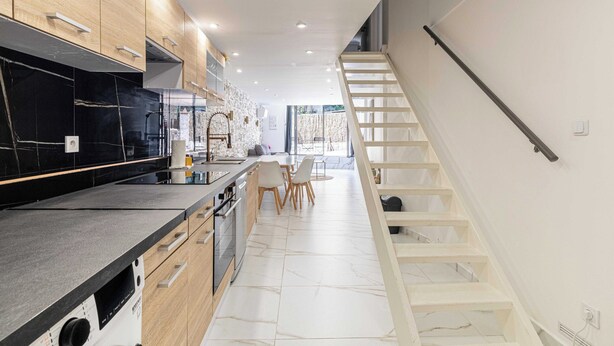 Een moderne keuken met houten kastjes, een zwart aanrecht en een witte trap.