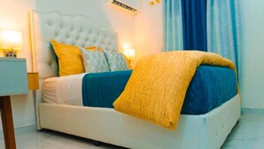 A neatly made bed with a white headboard, blue and yellow bedding, and a bedside table with a lamp.