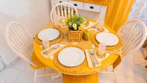 A round dining table with white plates, cutlery, and a woven placemat.