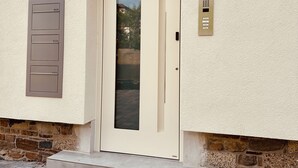 A beige door with a glass panel, a wall-mounted intercom, and a security camera.