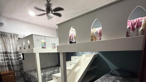Quarto com beliche, escorregador, ventoinha no teto e janela com cortinas.
