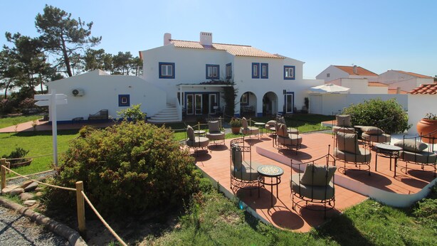 A white building with a tiled roof, outdoor seating area, and a well-maintained garden. - Quinta do Canal (Odemira)