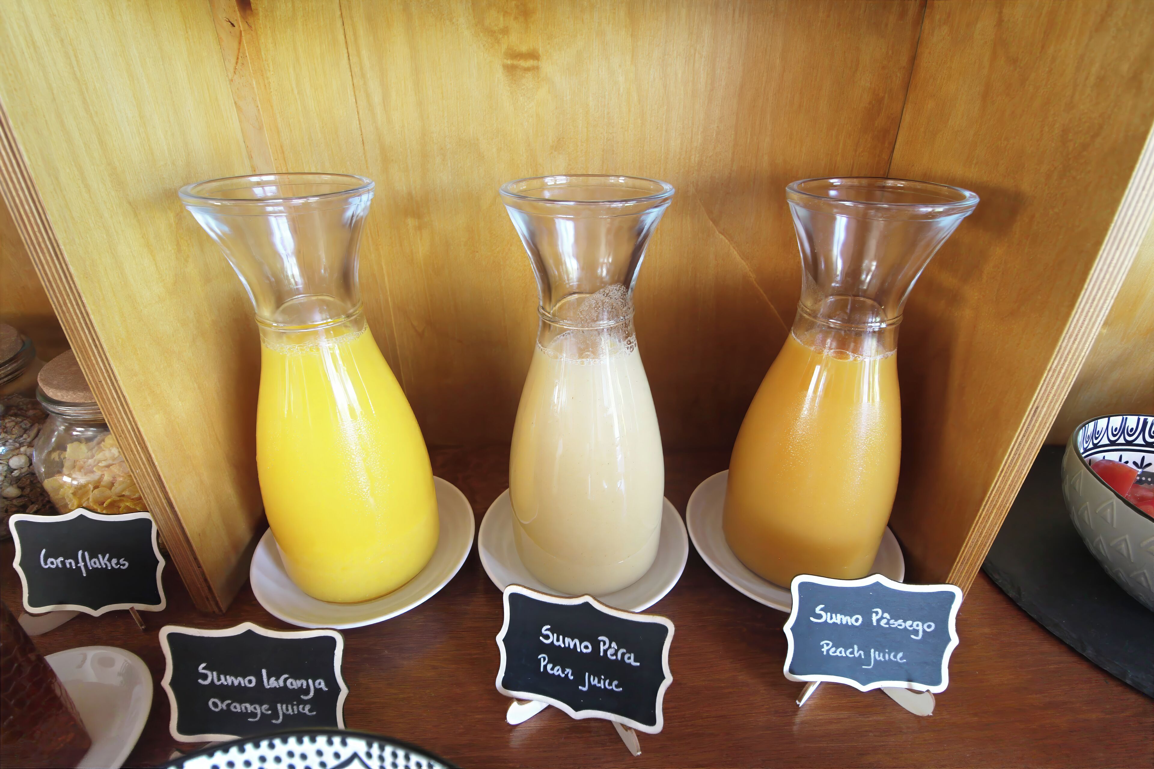 Eine Präsentation von drei Glasflaschen mit verschiedenen farbigen Säften, beschriftet mit Cornflakes, Orangensaft und Pfirsichsaft.