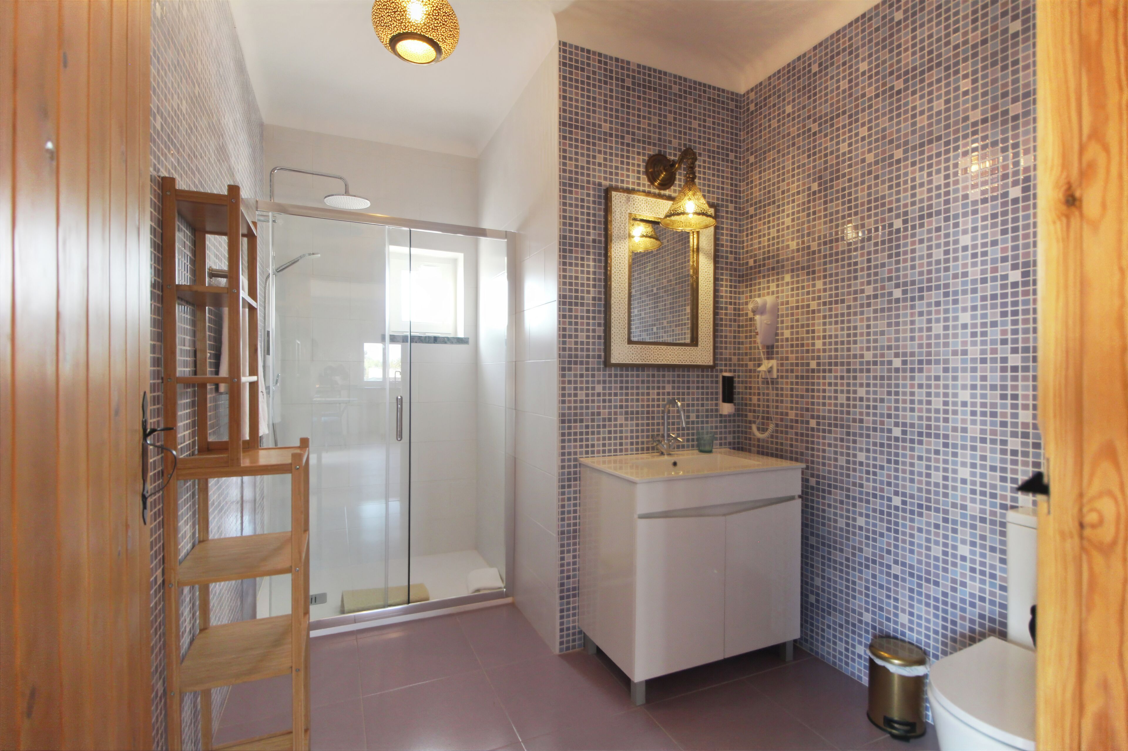 Un baño con cabina de ducha de vidrio, lavabo blanco y pared revestida de azulejos con un espejo.