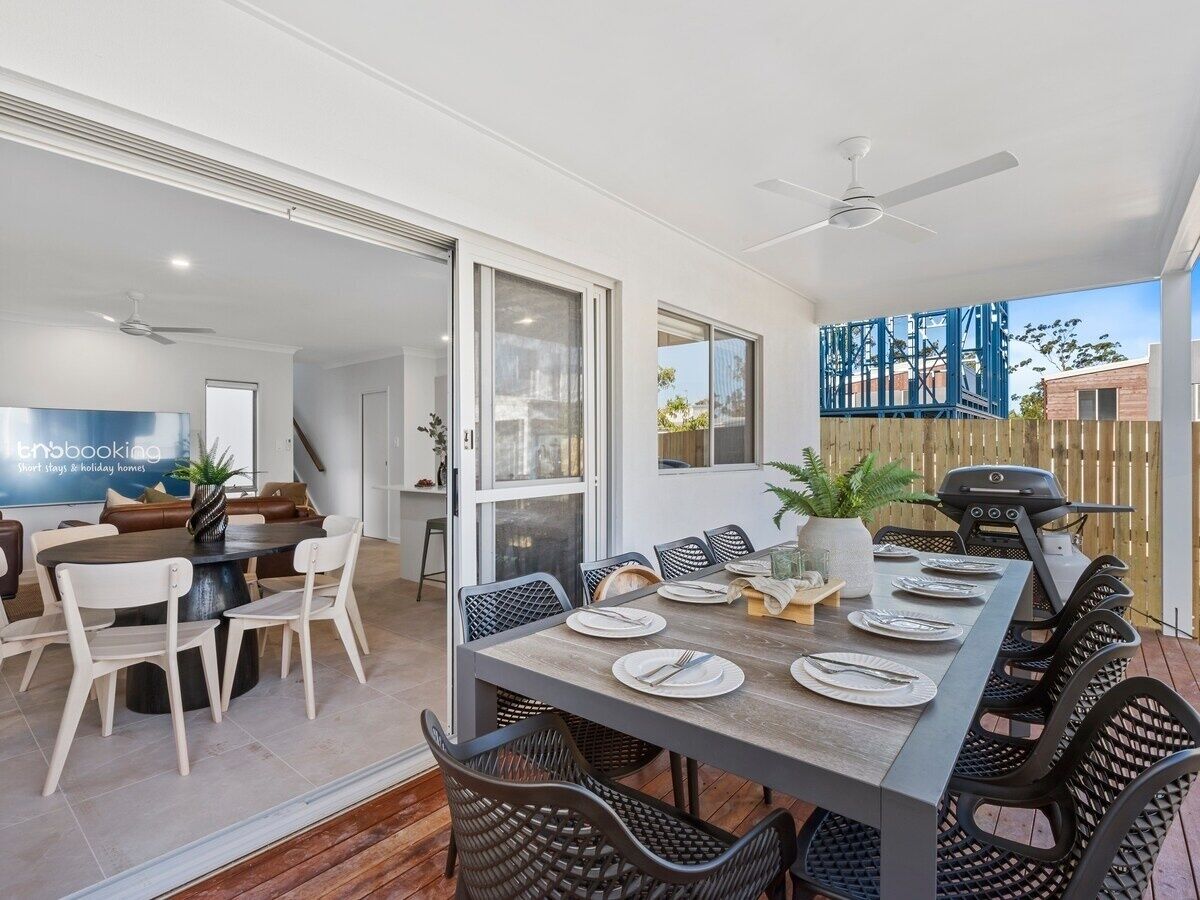 A dining area with a long table set for six, surrounded by chairs, and a grill outside.