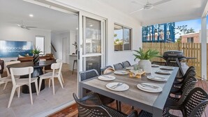 Een eethoek met een lange tafel gedekt voor zes personen, omringd door stoelen, en een barbecue buiten.