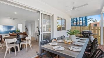 A dining area with a long table set for six, surrounded by chairs, and a grill outside.