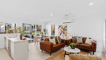 A modern living space with a kitchen island, a brown leather sofa, a round coffee table, and a dining area with chairs.
