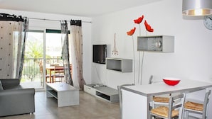 A modern living space with a sofa, dining table, chairs, a TV, a clock, and a red bowl. - Res. Marea Resort, Santa-lucia-di-moriani (Santa-Lucia-di-Moriani)