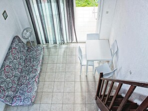 A small, enclosed patio with a white table and chairs, a patterned sofa, and a fan. - Res. Marea Resort, Santa-lucia-di-moriani (Santa-Lucia-di-Moriani)