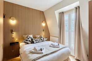 A modern hotel room with a sloped ceiling, a large bed with white linens, two wall-mounted lights, and a window with curtains. - Modern Studio Trocadero Tour Eiffel (Paris)