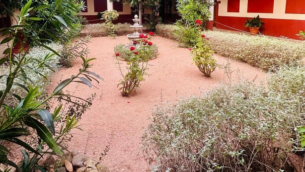 A courtyard with a central fountain, surrounded by greenery and red buildings.