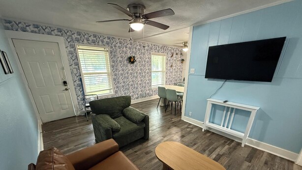 Una sala de estar con un sofá de cuero marrón, un sillón verde, una mesa de centro de madera y un televisor de pantalla plana montado en la pared.