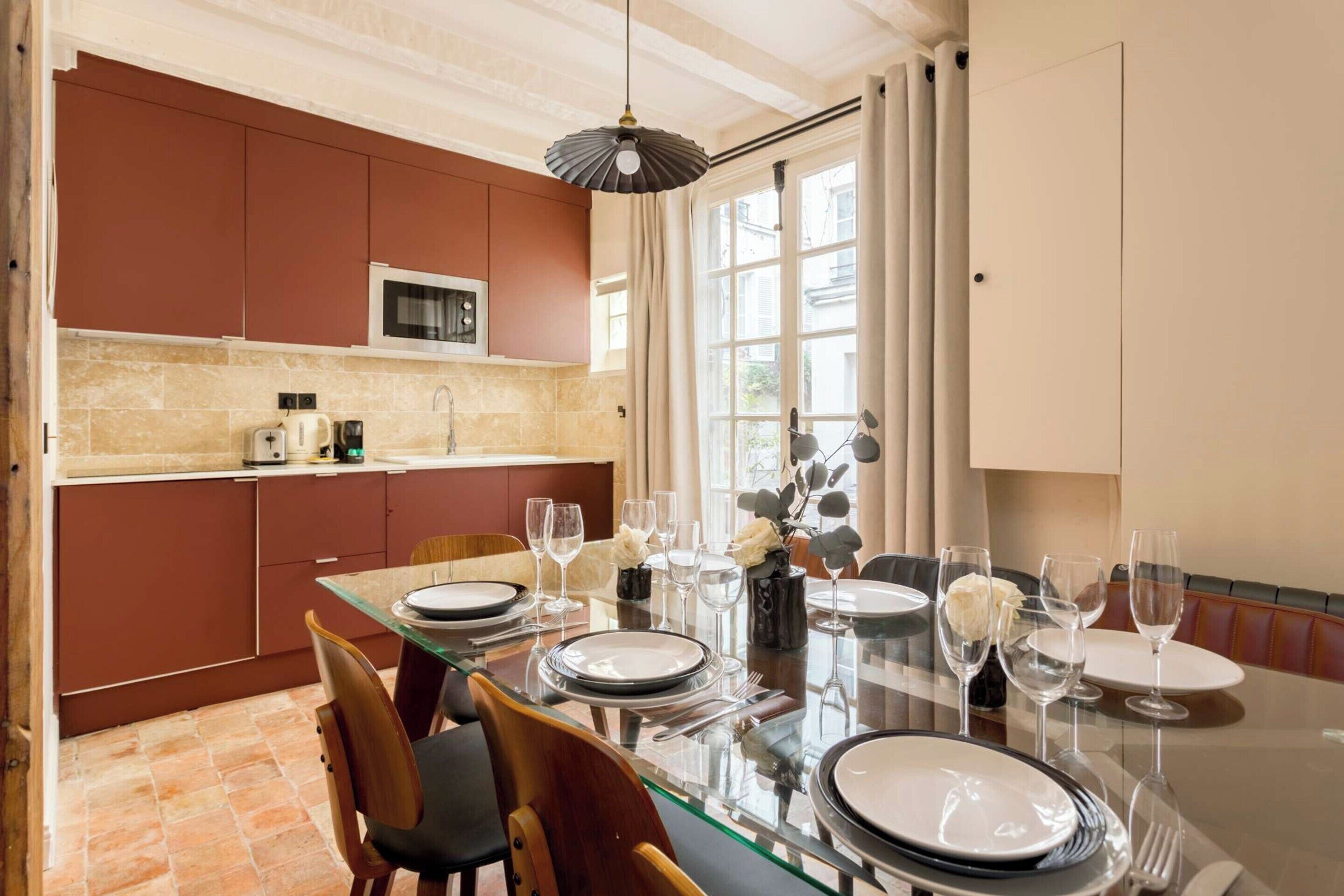 A dining area with a glass table set for four, surrounded by wooden chairs.
