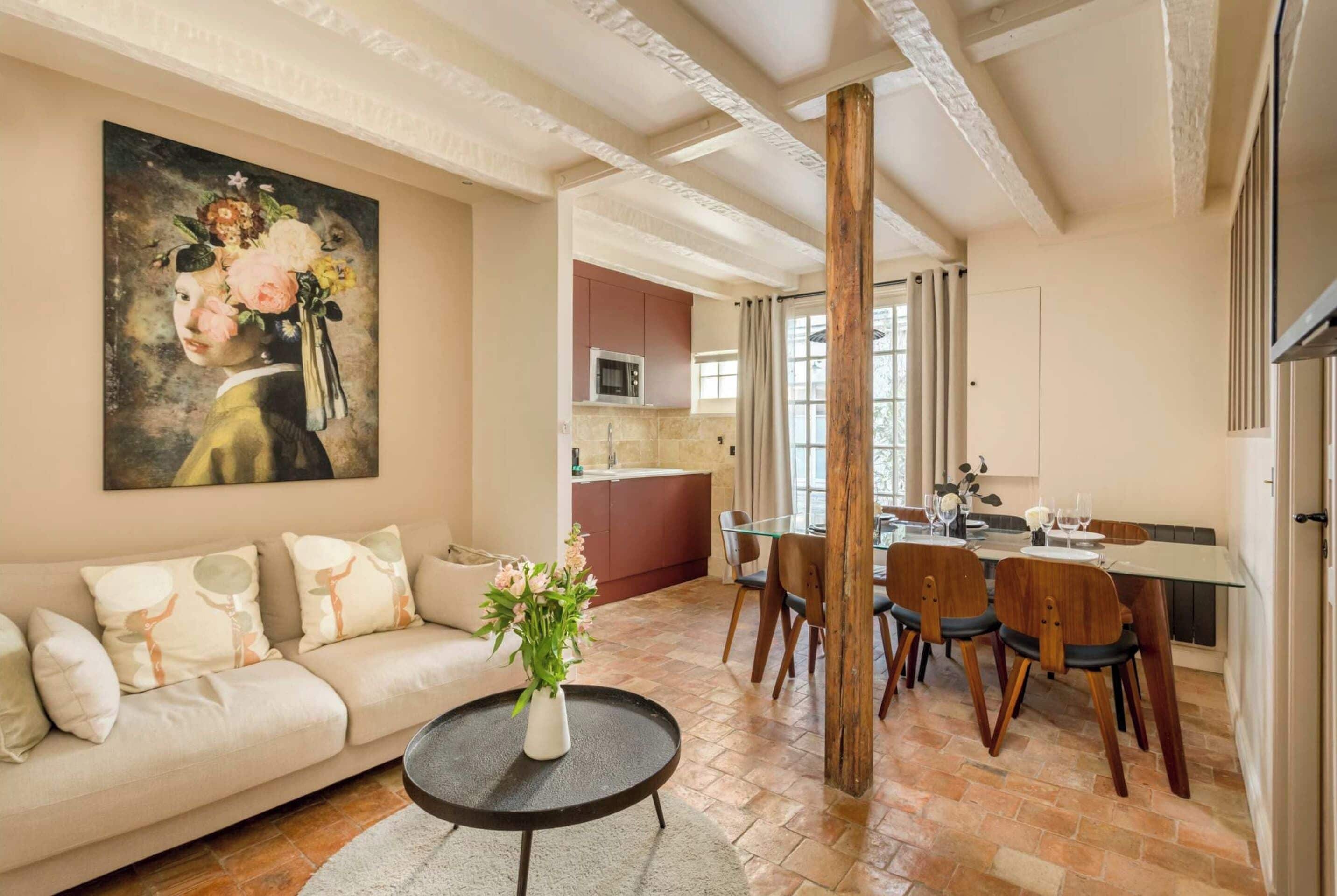 A living room with a sofa, a coffee table with a vase, a dining area with chairs and a table, and a kitchen in the background.