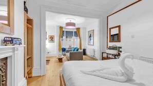 Une chambre d’hôtel avec un grand lit, un plancher en bois, une cheminée, un bureau, une chaise, une fenêtre avec des rideaux et une salle de bain avec un miroir et un lavabo.