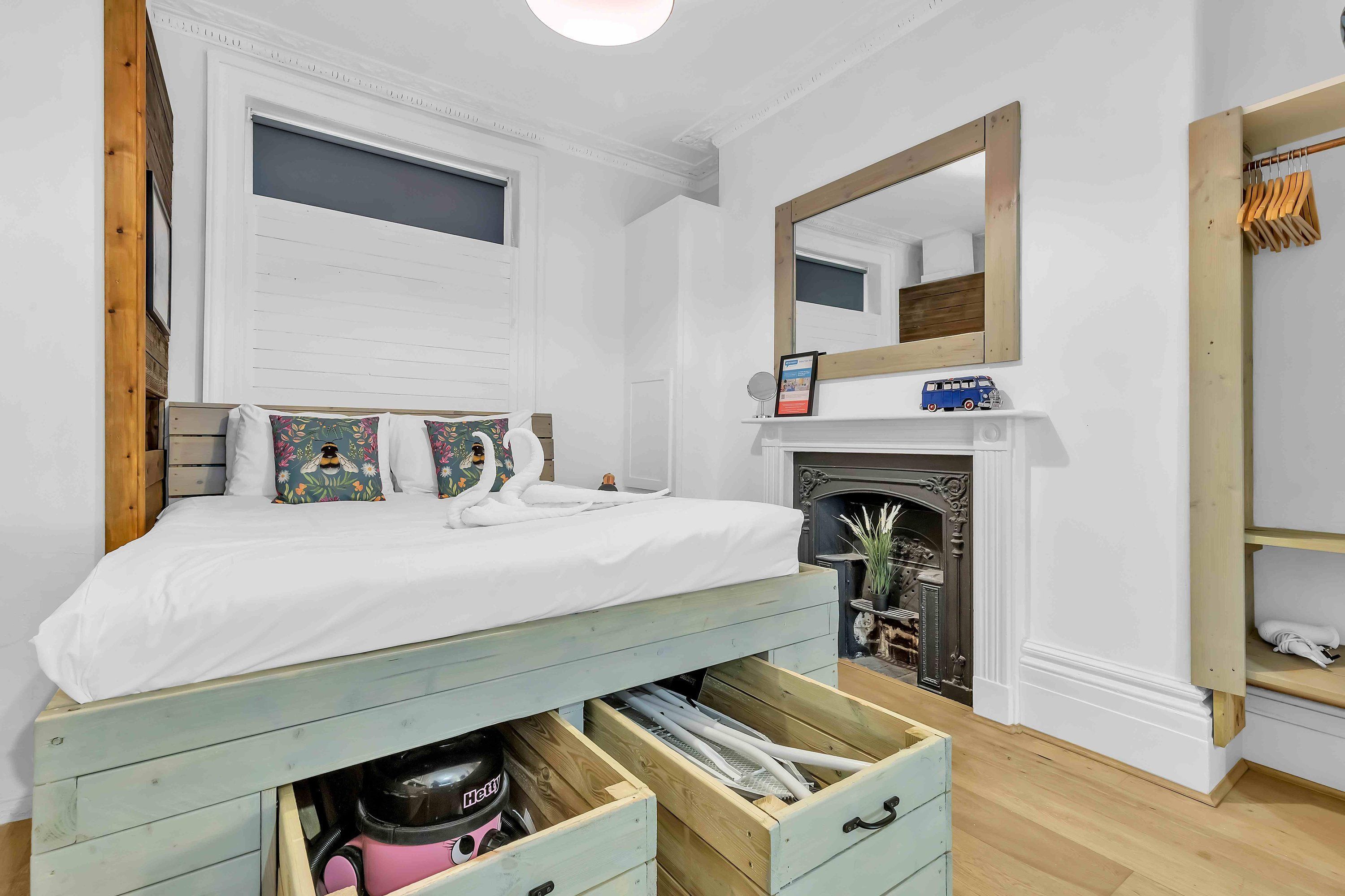 A bedroom with a bed, a wooden headboard, a fireplace, a mirror, and a shelf with towels.